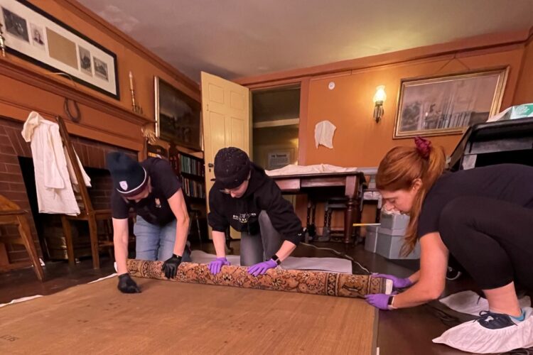 National Park Service curators rolling a historic 19th-century rug at The Wayside: Home of Authors during spring cleaning.