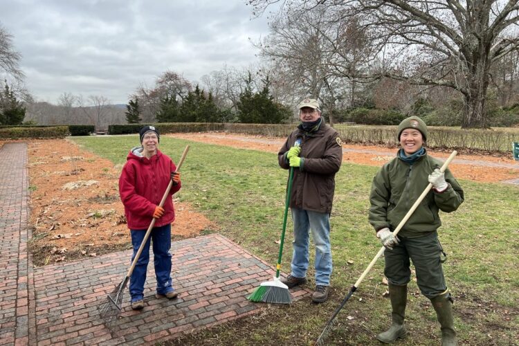 Three volunteers with rakes stand before the gardens which are mulched with pine needles.